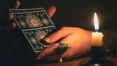 Vrouw schudt tarotkaarten in een donkere ruimte, verlicht door een kaars